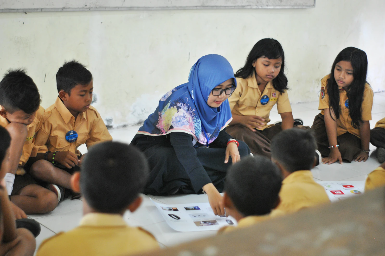 A teacher in a headscarf guiding pupils sitting on a classroom floor